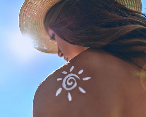 femme au soleil qui se protège d'un coup de soleil avec une protection solaire et un chapeau